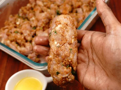 Apply oil on your hands, take one portion of chicken mixture, make a cylindrical shape, use two hands to form long cylindrical shape around the skewer